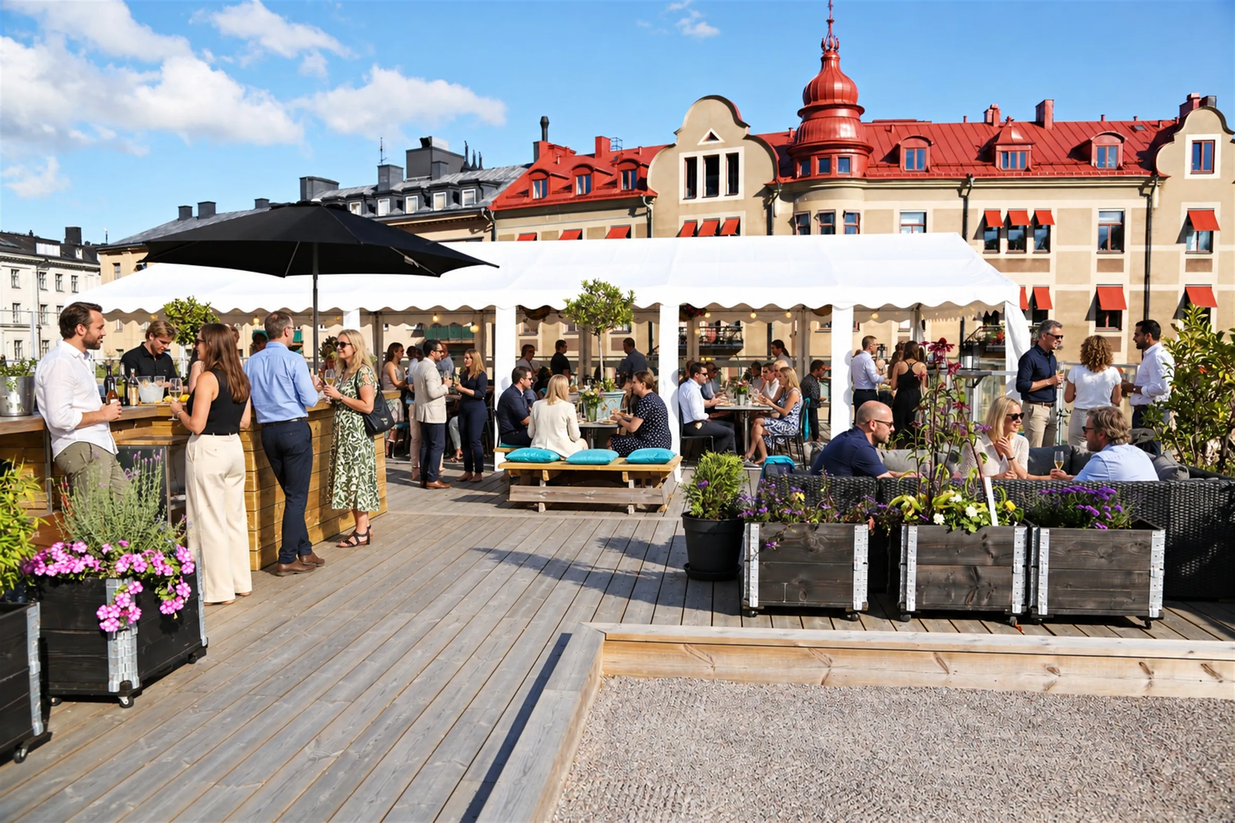 Gäster minglar med vinglas på en takterrass i solsken, med bar, vita partytält och Vasastans tak bakom.