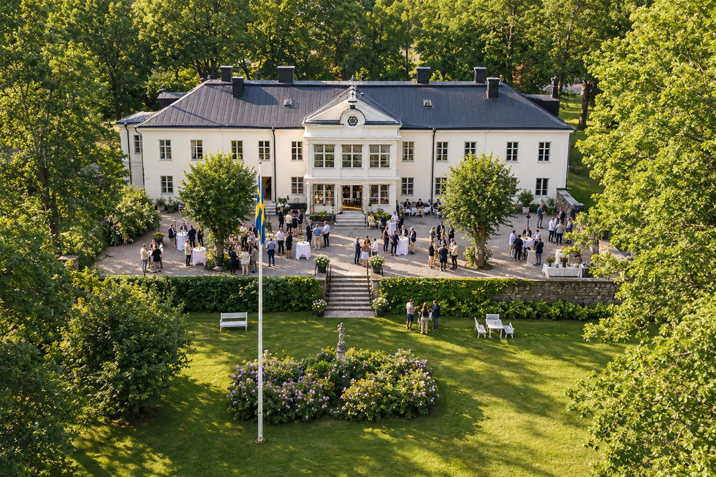 Ett sextiotal gäster minglar vid ståbord på grusgården framför Elfviks gårds vita huvudbyggnad, sett uppifrån.