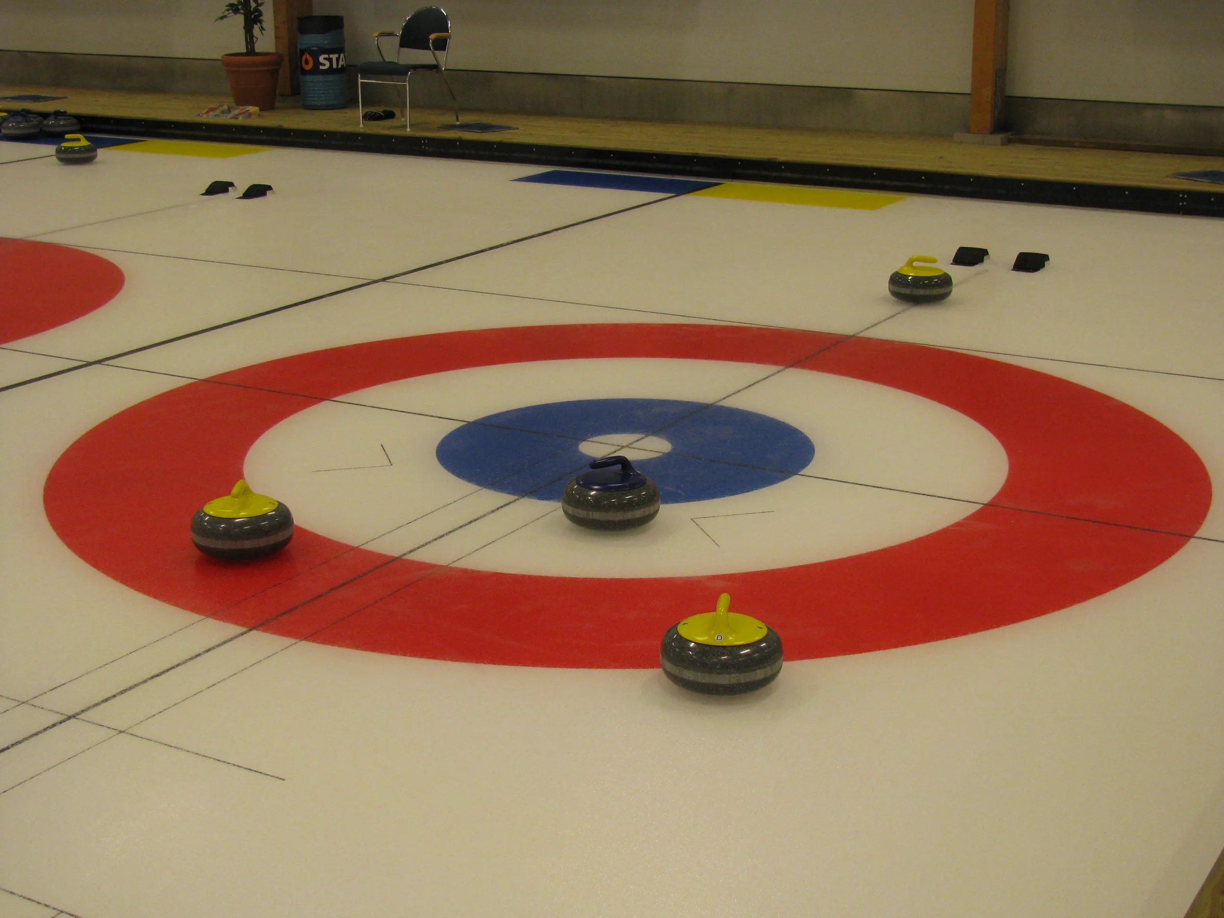 Curlingstenar med gula och röda handtag ligger i det röda och blå boet på en blank curlingbana.