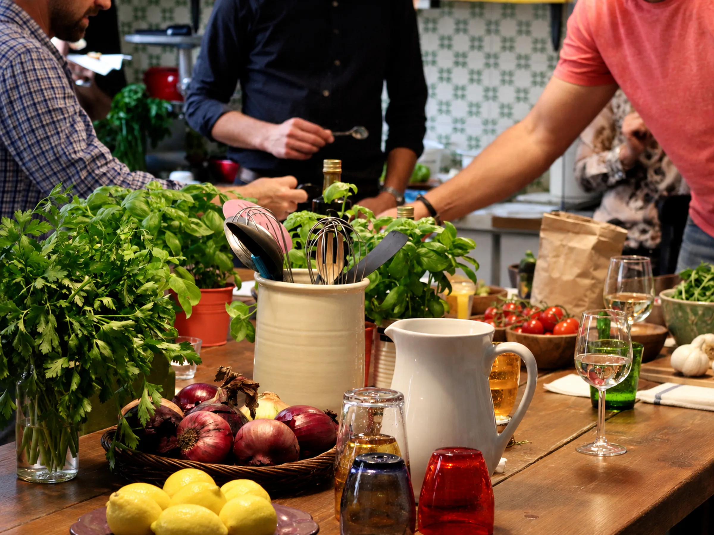 Färska grönsaker, örter och kantareller på ett köksbord medan deltagare lagar mat i bakgrunden.