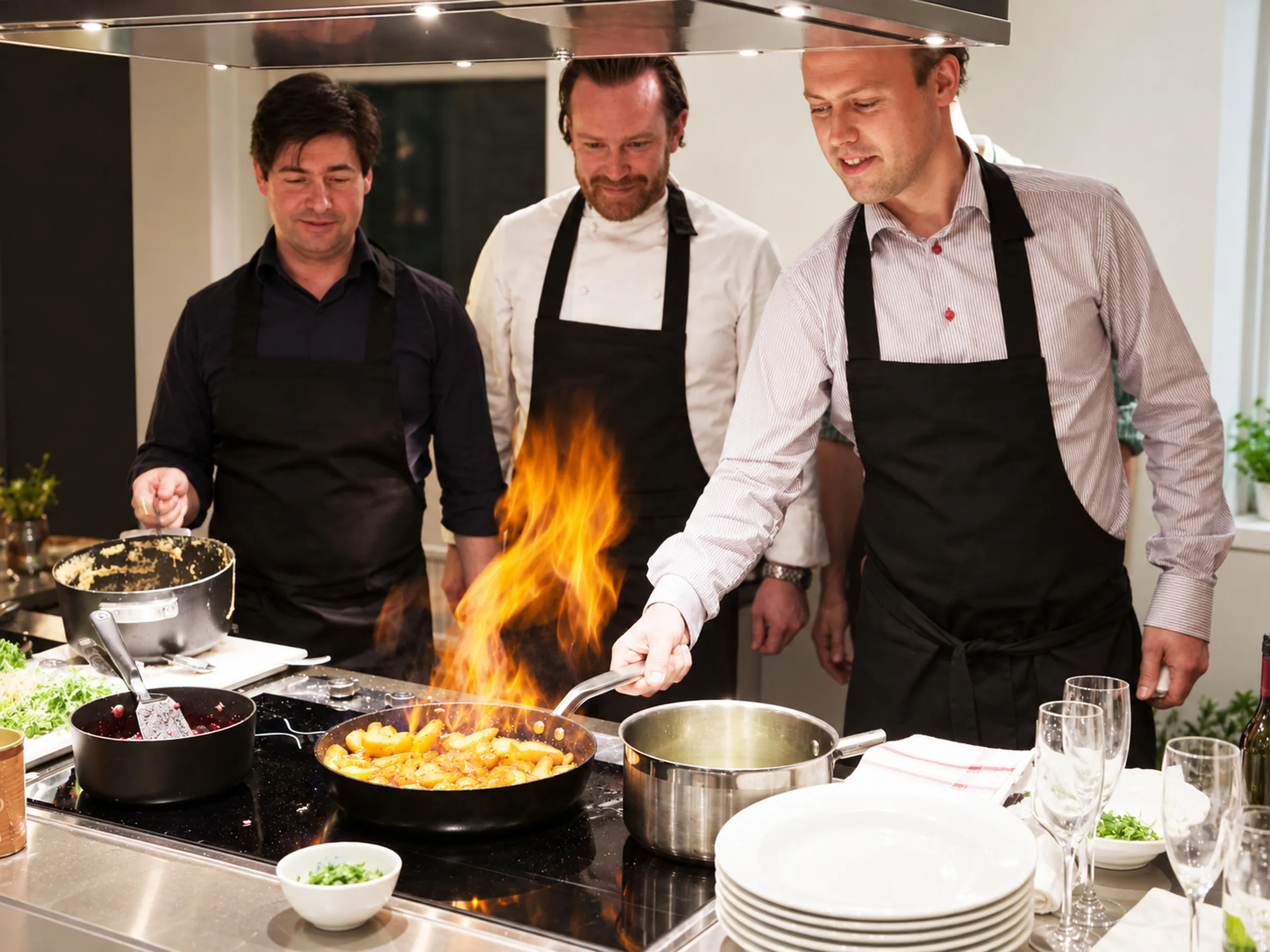 En kock flamberar i stekpannan medan deltagare i förkläden tittar på i ett restaurangkök.