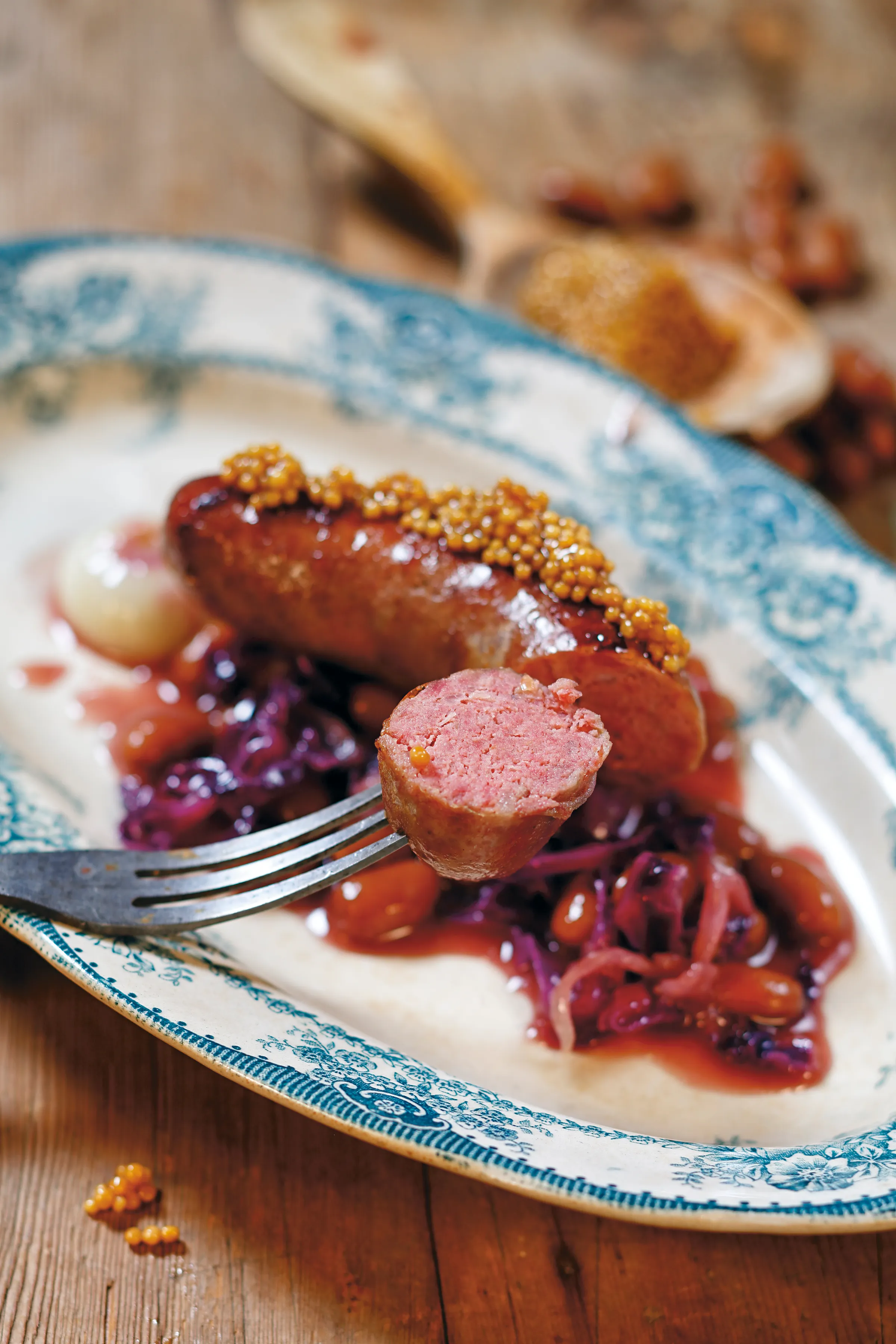 Grillad vildsvinskorv med senapsfrön, rödkål och lingon på en blåmönstrad tallrik av äldre modell.