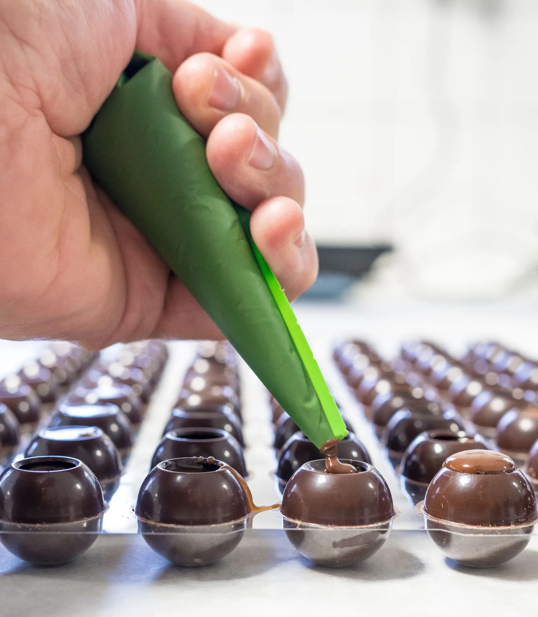 En hand fyller pralinskal av mörk choklad med kola ur en spritspåse.