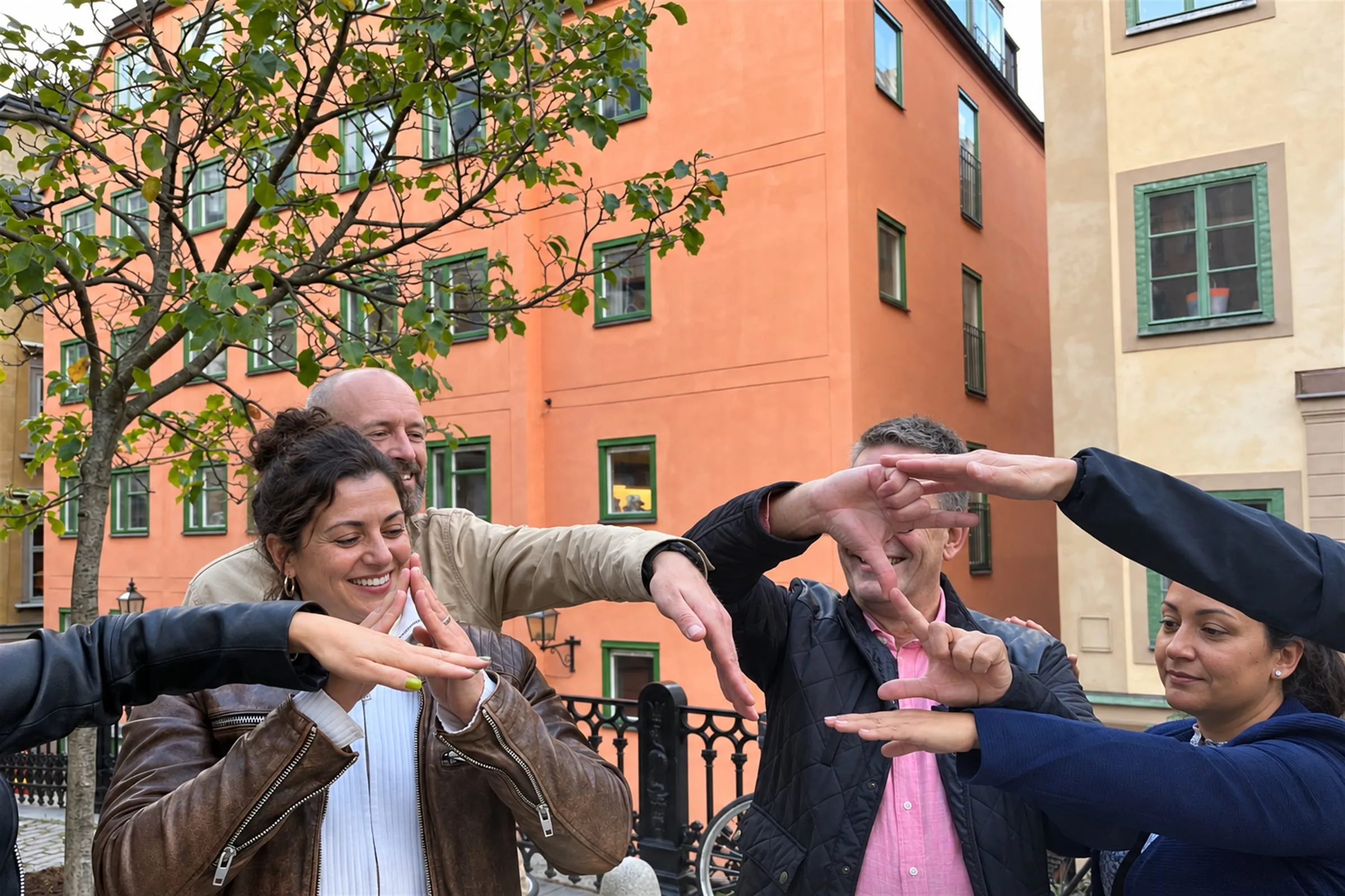 Kollegor gestikulerar glatt tillsammans under en aktivitet bland färgglada fasader i Gamla stan.