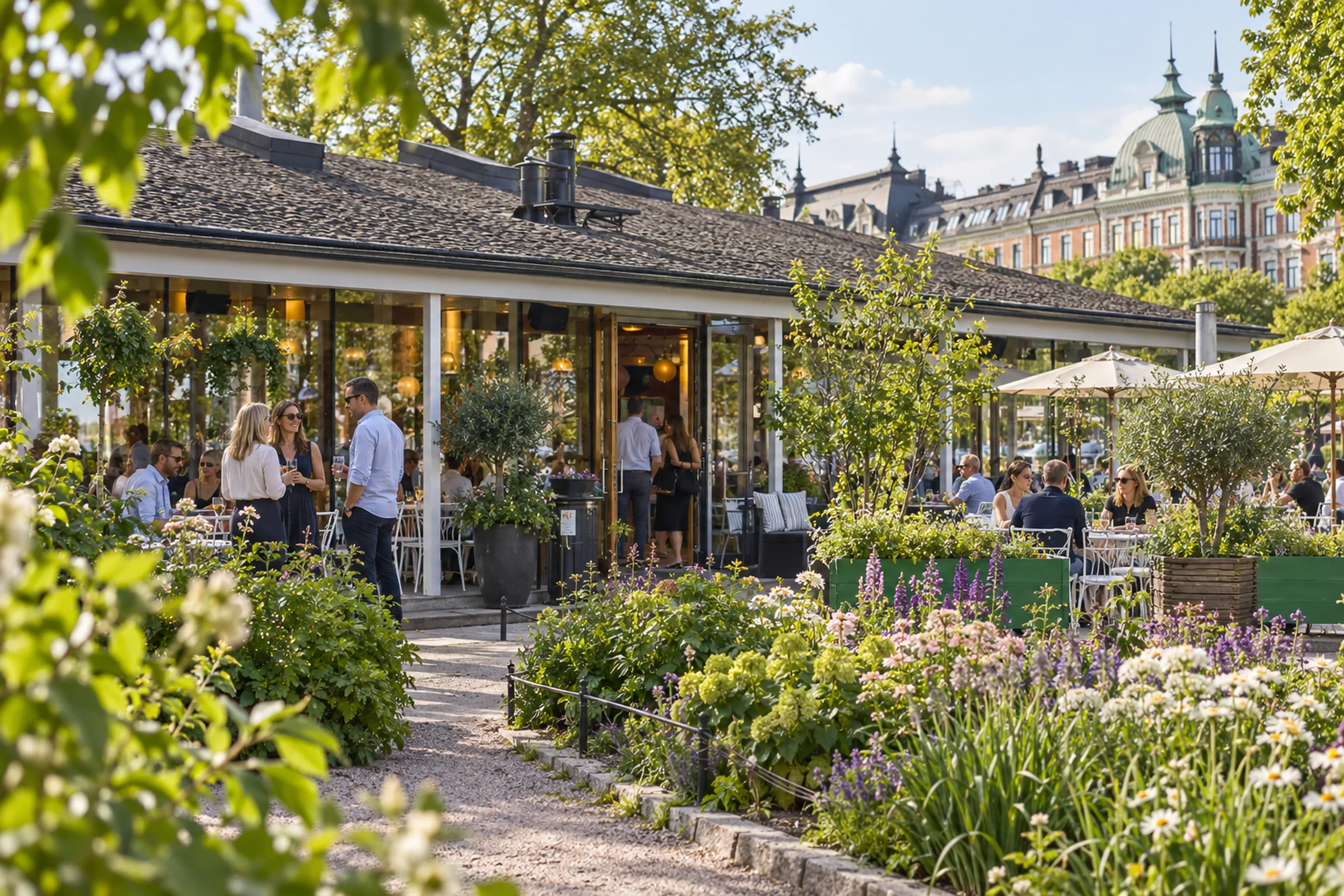 Kollegor minglar på en grönskande uteservering framför en glasad restaurangpaviljong en solig sommarkväll.